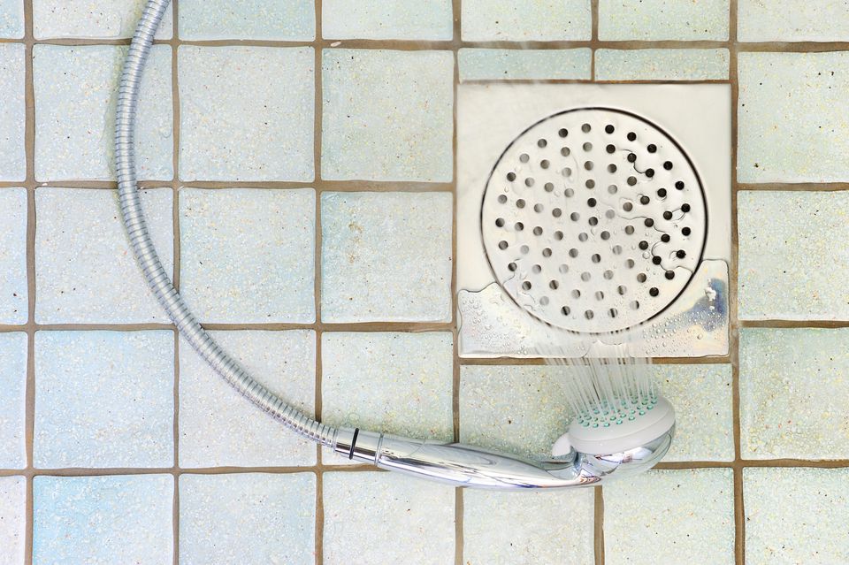 A detachable shower head pouring water down a drain.